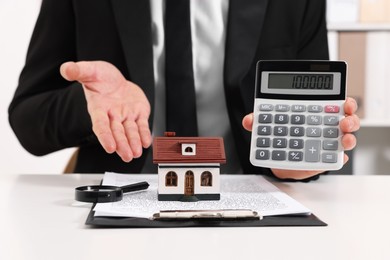 Photo of Real estate agent showing calculator with price for house at white table in office, closeup. Home appraisal