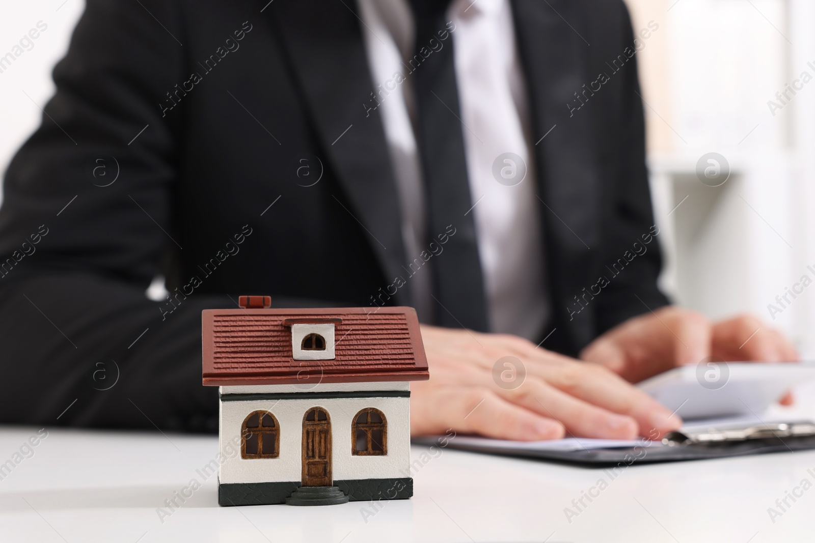 Photo of House figure and real estate agent with calculator at white table in office, selective focus. Home appraisal