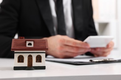 Photo of House figure and real estate agent with calculator at white table in office, selective focus. Home appraisal