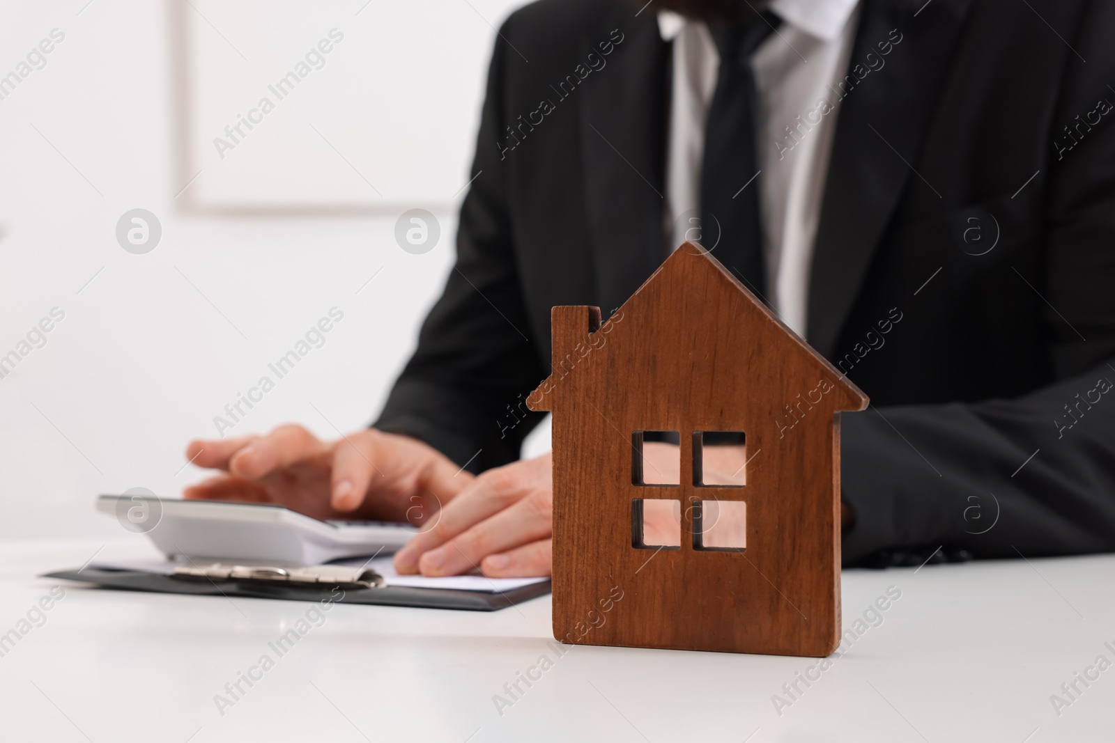 Photo of House figure and real estate agent with calculator at white table in office, selective focus. Home appraisal