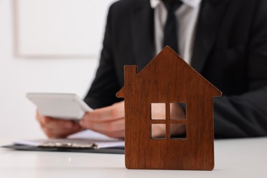 Photo of House figure and real estate agent with calculator at white table in office, selective focus. Home appraisal