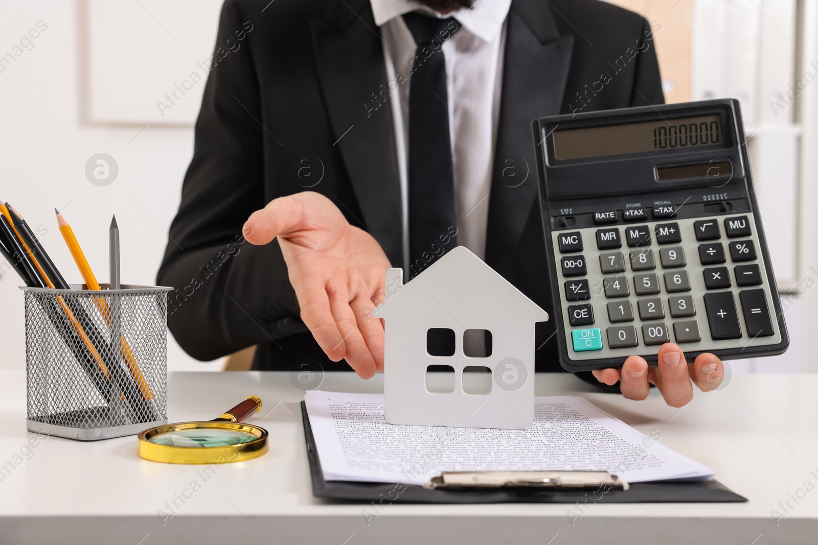 Photo of Real estate agent showing calculator with price for house at white table in office, closeup. Home appraisal