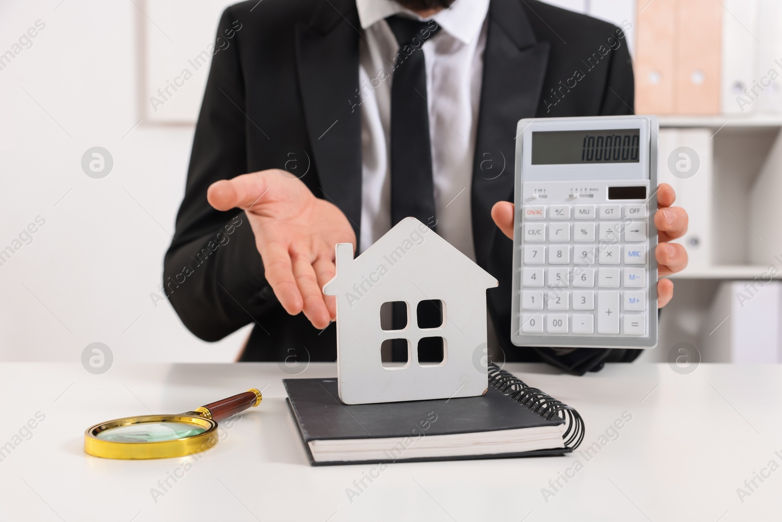 Photo of Real estate agent showing calculator with price for house at white table in office, closeup. Home appraisal