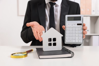 Photo of Real estate agent showing calculator with price for house at white table in office, closeup. Home appraisal