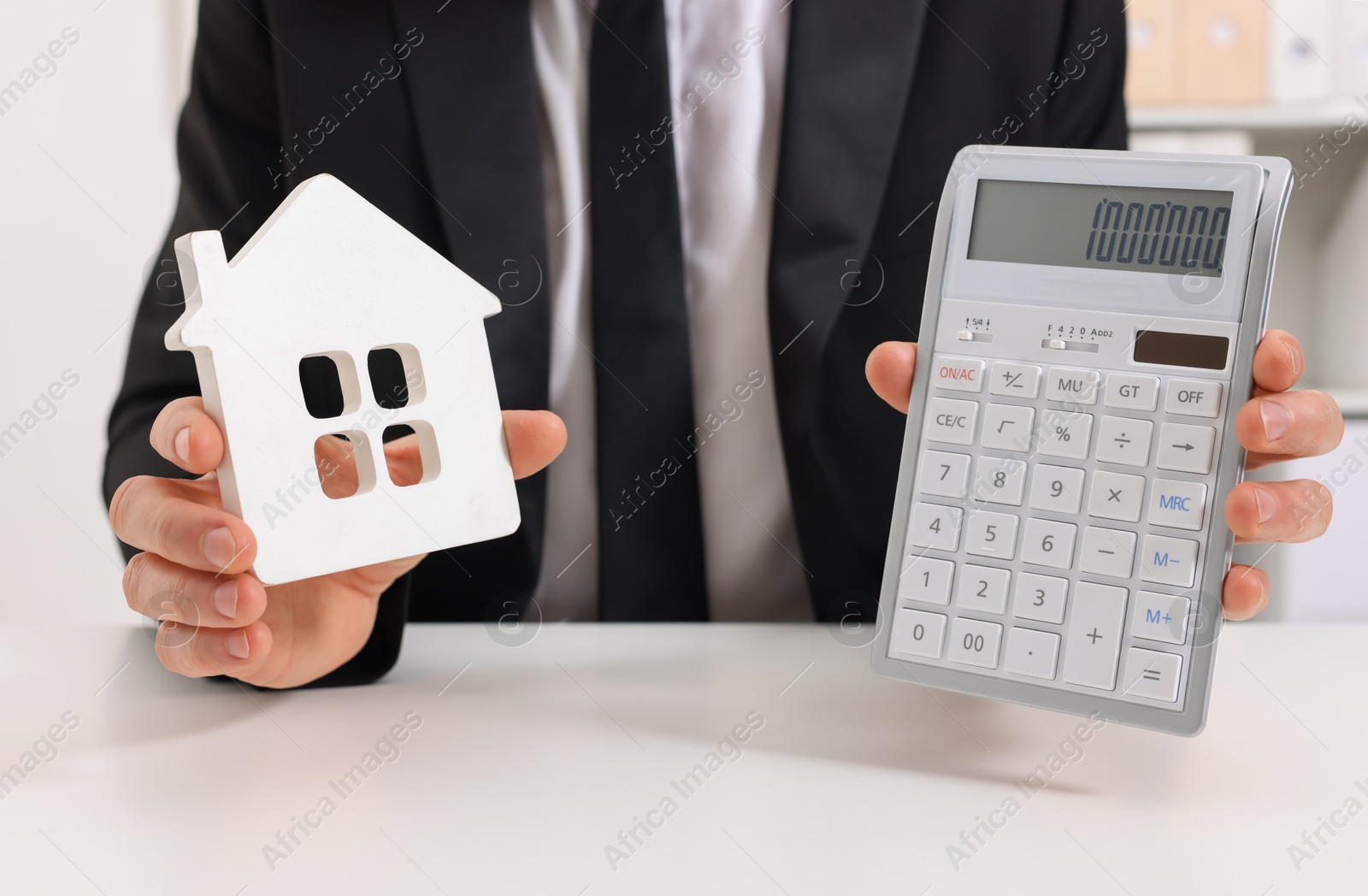 Photo of Real estate agent showing calculator with price for house at white table in office, closeup. Home appraisal