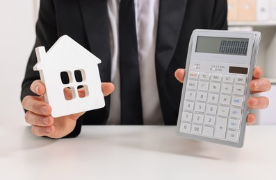 Photo of Real estate agent showing calculator with price for house at white table in office, closeup. Home appraisal