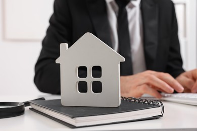 Real estate agent with calculator at white table in office, focus on house figure and notepad. Home appraisal