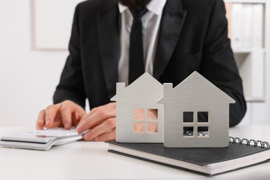 Photo of Real estate agent with calculator at white table in office, focus on house figures and notepad. Home appraisal