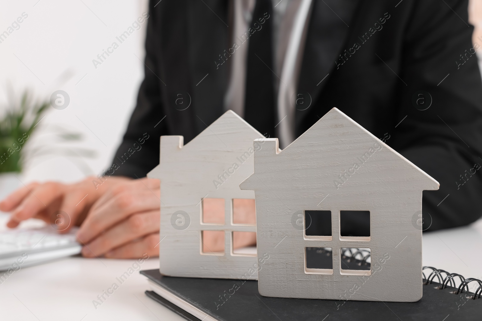 Photo of Real estate agent with calculator at white table in office, focus on house figures and notepad. Home appraisal