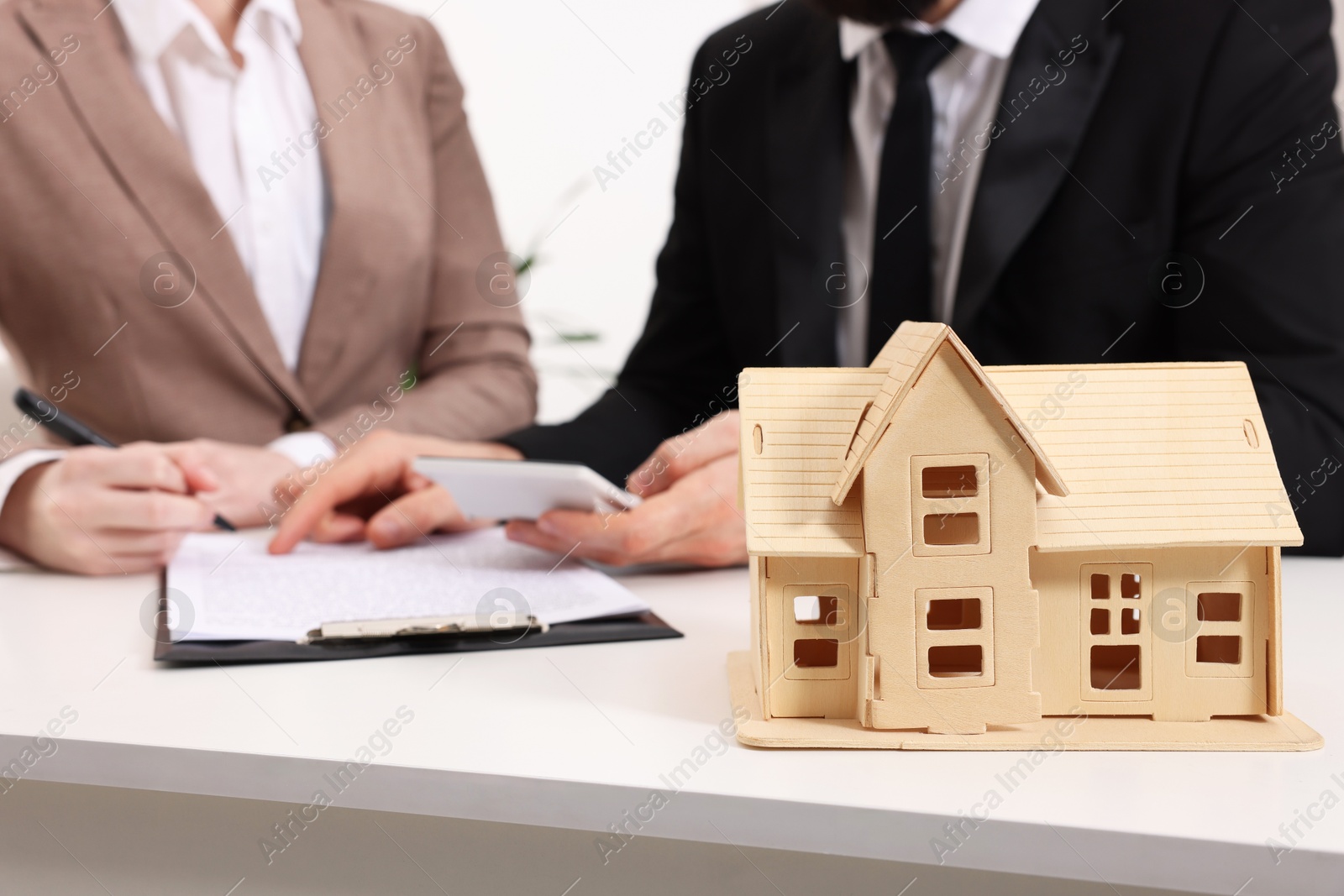 Photo of Real estate agent showing client where to sign document at white table in office, focus on house figure. Home appraisal