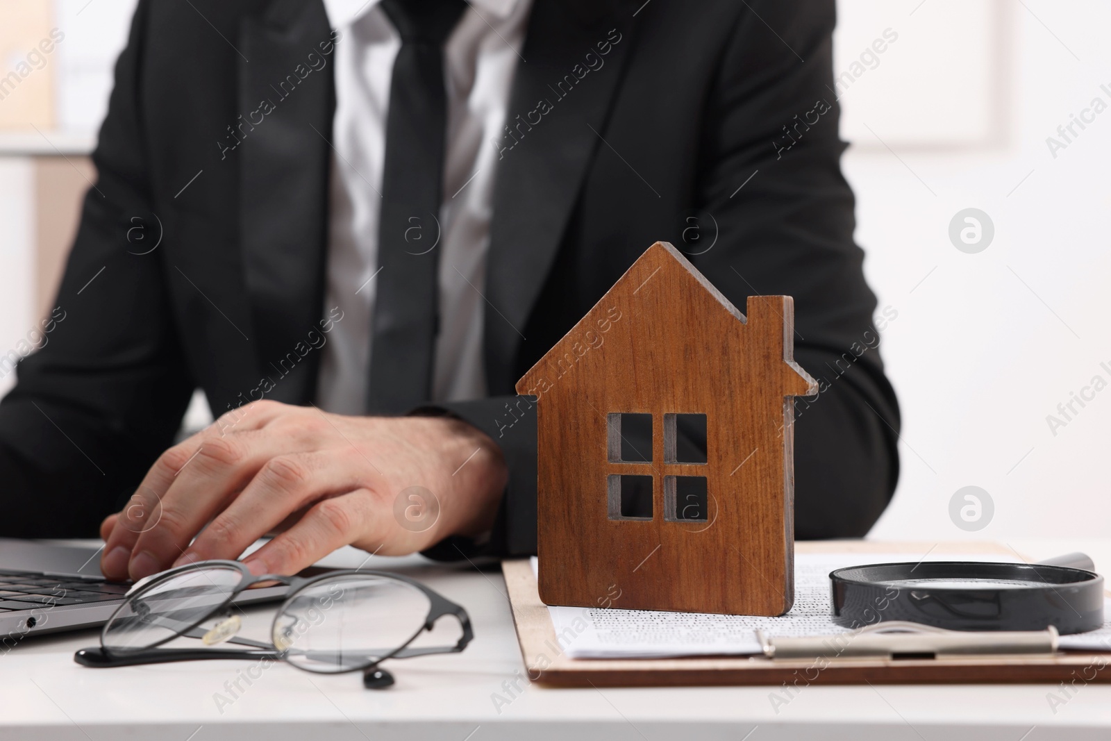 Photo of Real estate agent working with laptop at white table with house figure in office, closeup. Home appraisal