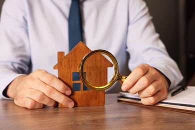 Photo of Real estate agent with house figure and magnifying glass at wooden table, closeup. Home appraisal