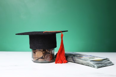 Photo of Graduate hat, dollar banknotes and coins on white marble table, closeup. Tuition payment