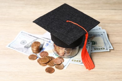 Photo of Graduate hat, dollar banknotes and coins on wooden table, closeup. Tuition payment