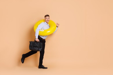 Photo of Businessman with inflatable ring and briefcase on beige background, space for text