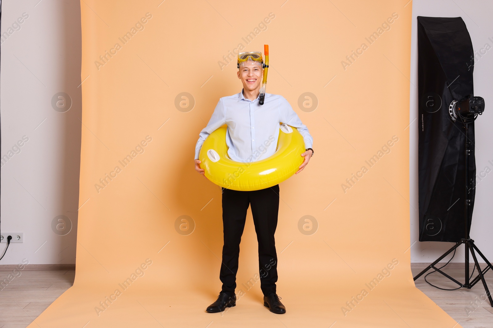 Photo of Businessman with inflatable ring and snorkeling equipment on beige background