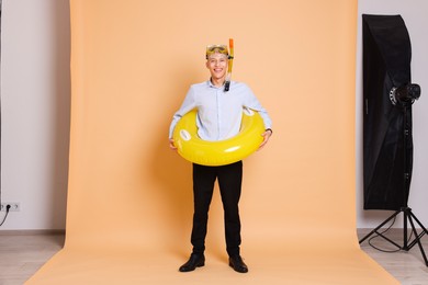 Businessman with inflatable ring and snorkeling equipment on beige background