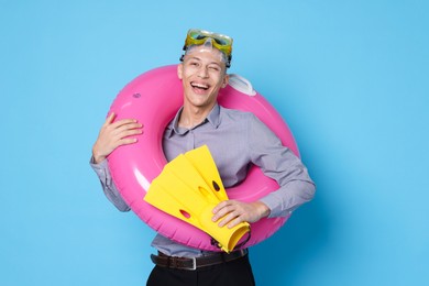 Photo of Businessman with inflatable ring, flippers and diving mask on light blue background