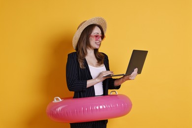 Photo of Businesswoman with inflatable ring, straw hat, sunglasses and laptop on orange background