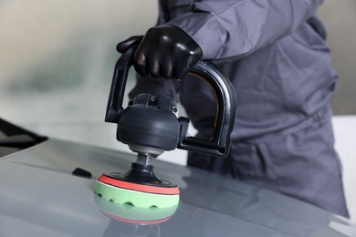 Photo of Man polishing car hood with orbital polisher indoors, closeup