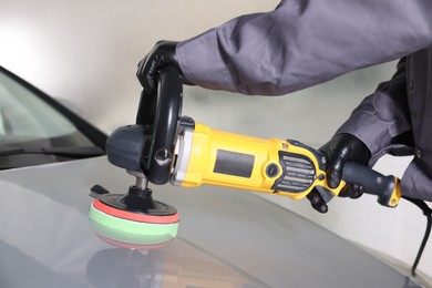 Photo of Man polishing car hood with orbital polisher indoors, closeup