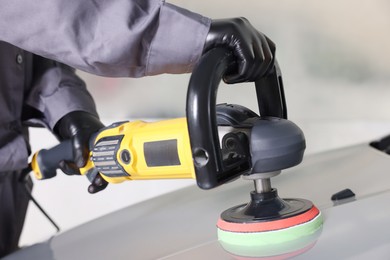 Photo of Man polishing car hood with orbital polisher indoors, closeup