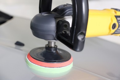 Photo of Man polishing car hood with orbital polisher indoors, closeup