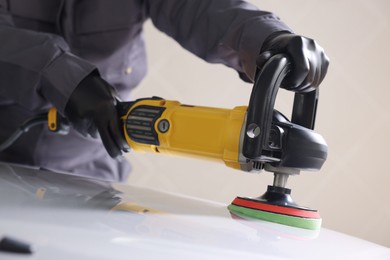 Photo of Man polishing car hood with orbital polisher indoors, closeup