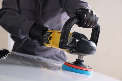 Photo of Man polishing car hood with orbital polisher indoors, closeup