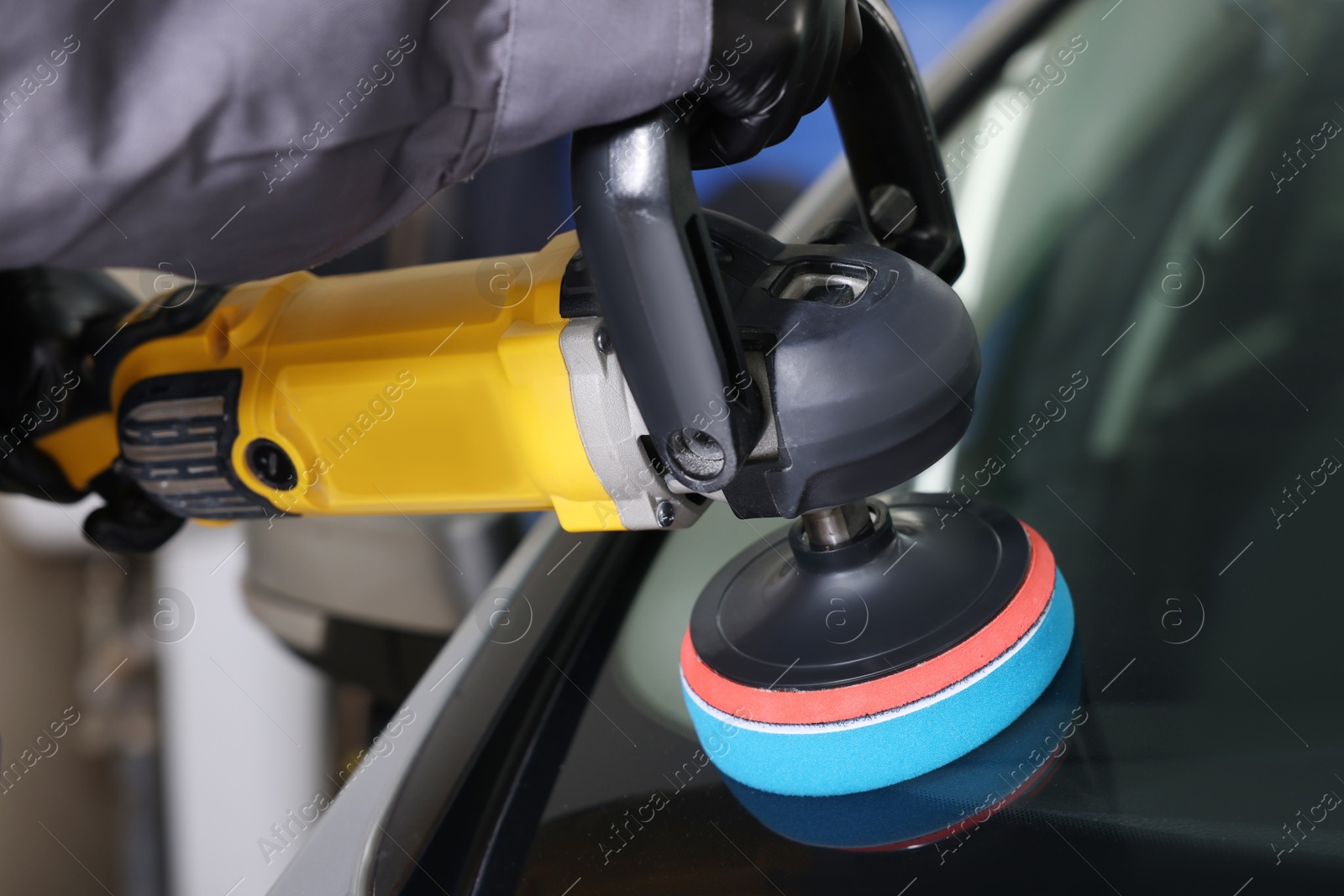 Photo of Man polishing car windshield with orbital polisher indoors, closeup