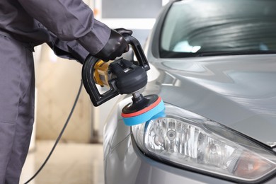 Photo of Man polishing car headlight with orbital polisher indoors, closeup