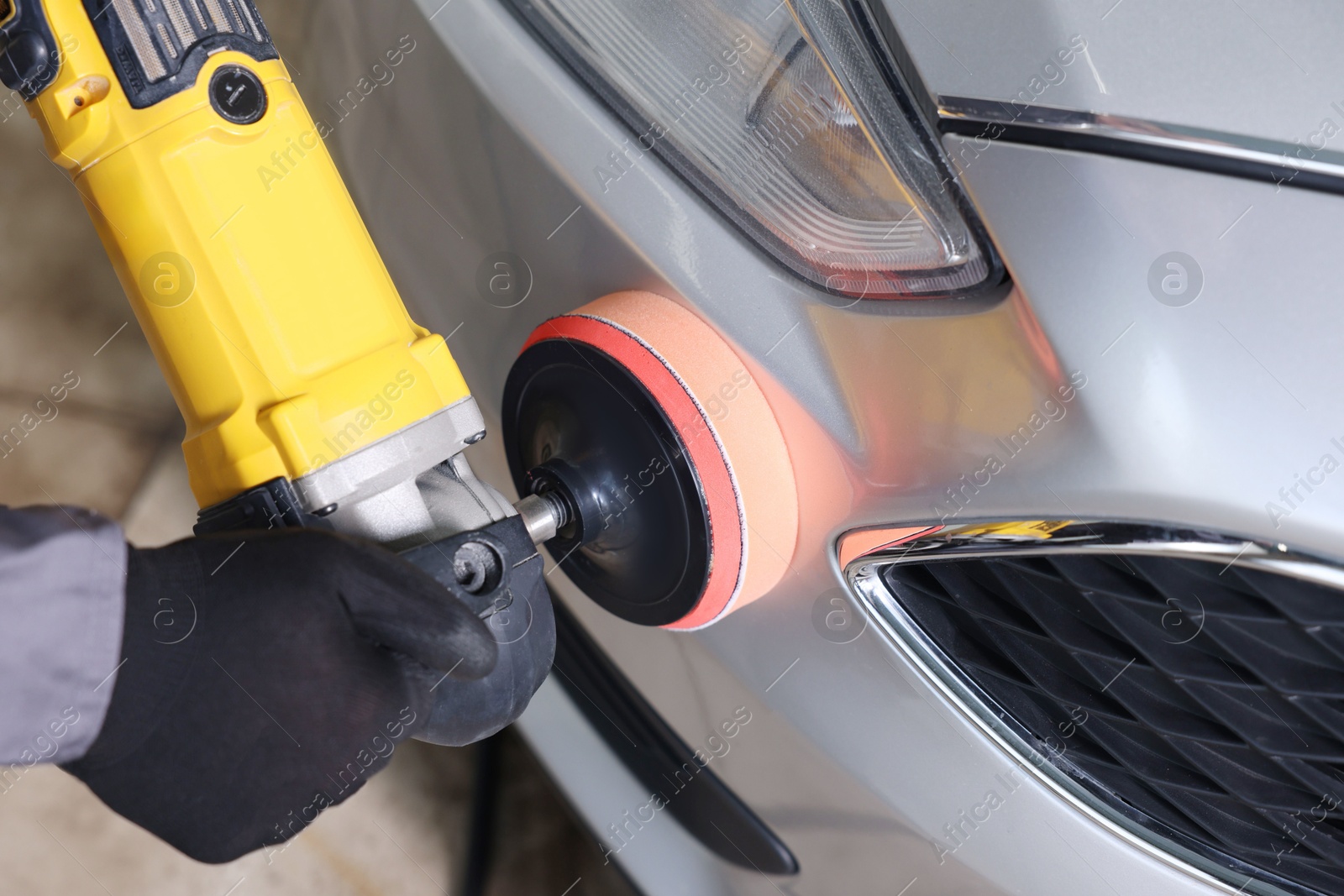 Photo of Man polishing car with orbital polisher indoors, closeup