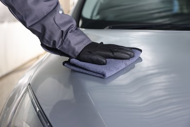 Photo of Man polishing car hood with rag indoors, closeup