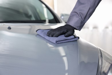 Photo of Man polishing car hood with rag indoors, closeup