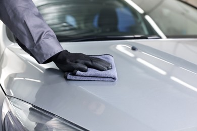 Photo of Man polishing car hood with rag indoors, closeup