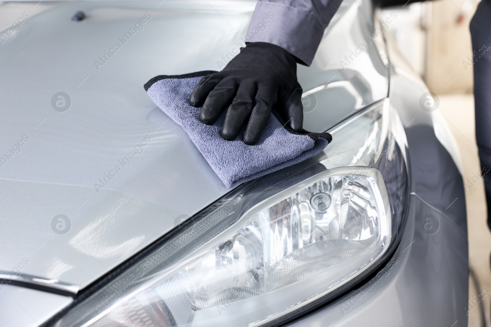 Photo of Man polishing car hood with rag indoors, closeup