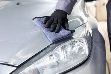 Photo of Man polishing car hood with rag indoors, closeup