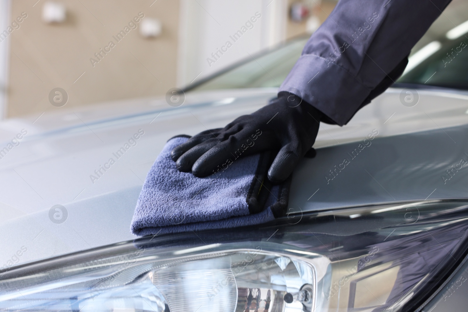 Photo of Man polishing car hood with rag indoors, closeup