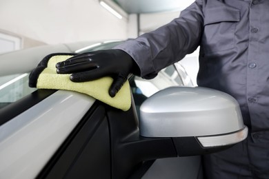 Photo of Man polishing car with yellow rag indoors, closeup