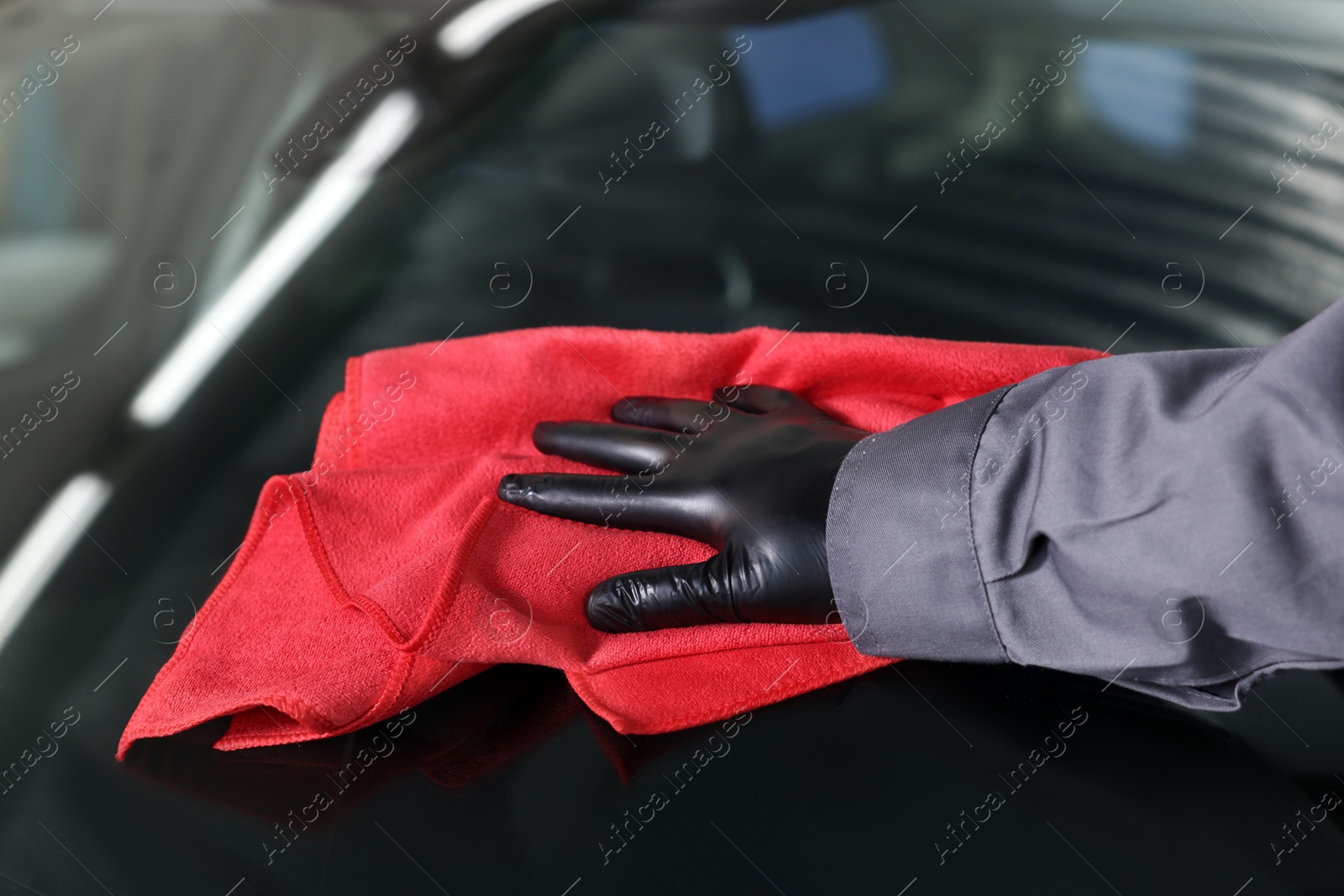 Photo of Man polishing car windshield with red rag indoors, closeup