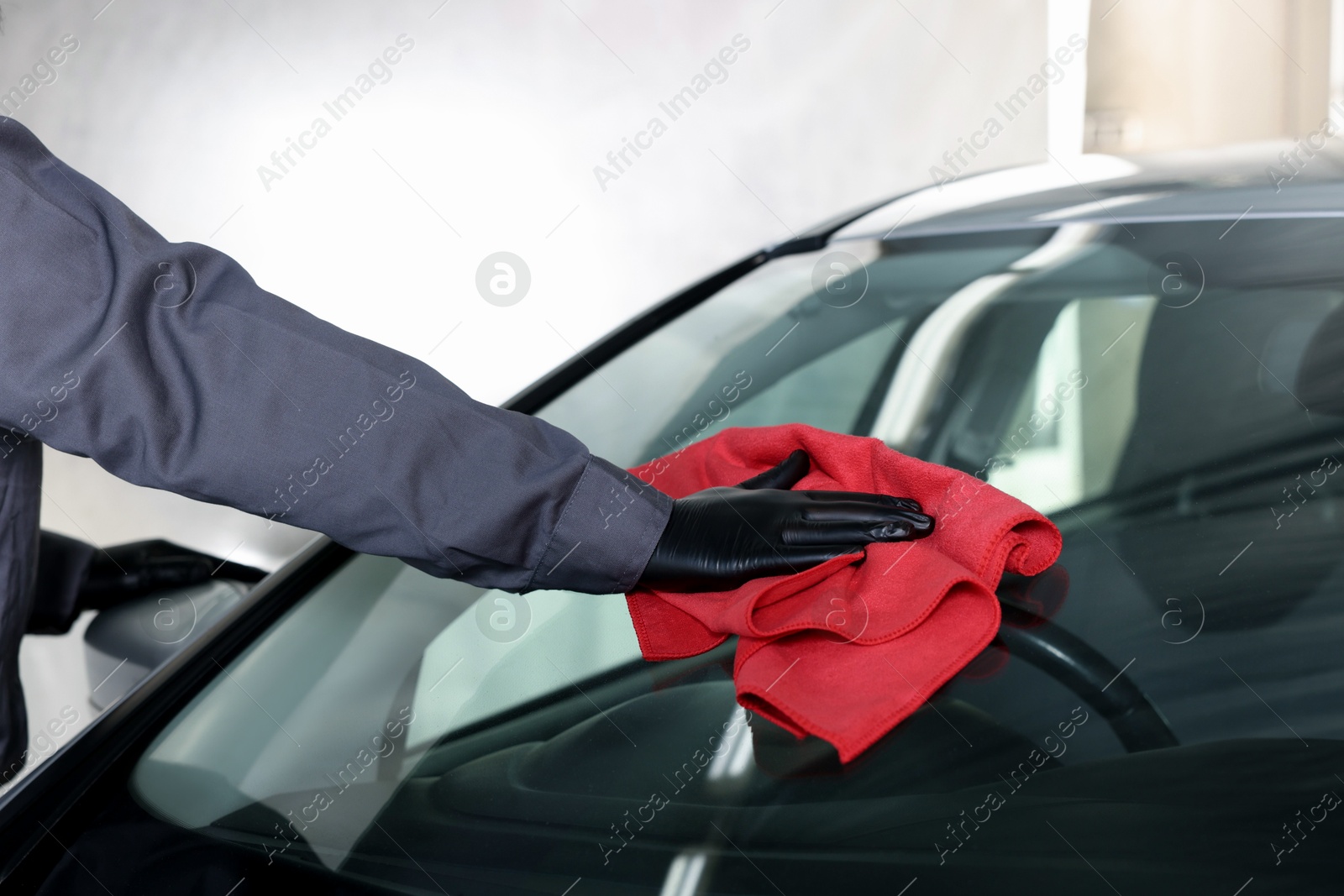 Photo of Man polishing car windshield with red rag indoors, closeup