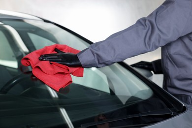 Photo of Man polishing car windshield with red rag indoors, closeup