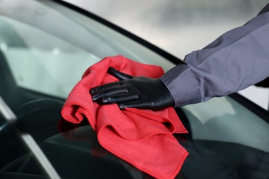 Photo of Man polishing car windshield with red rag indoors, closeup