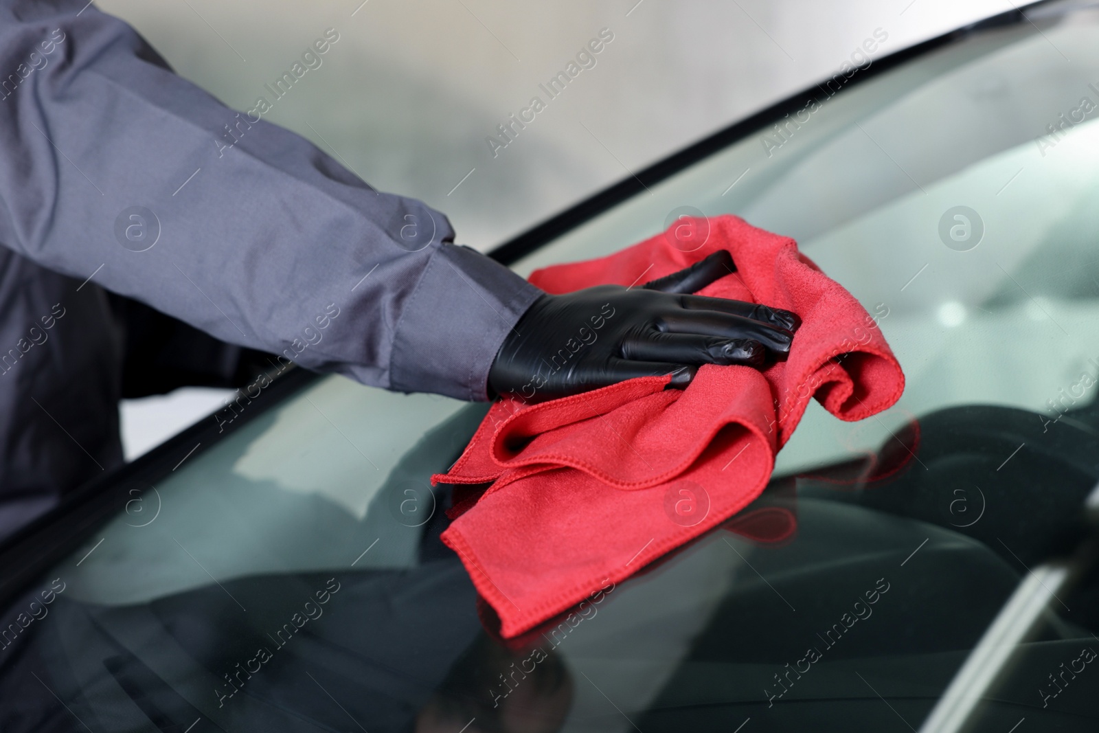 Photo of Man polishing car windshield with red rag indoors, closeup