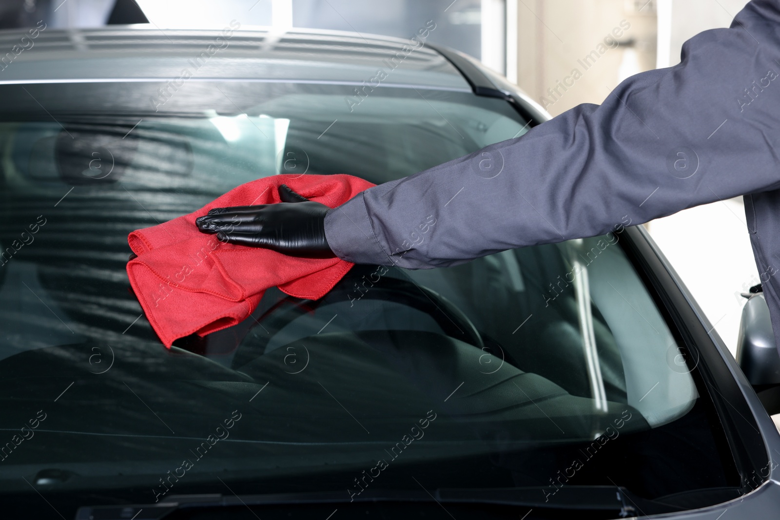 Photo of Man polishing car windshield with red rag indoors, closeup