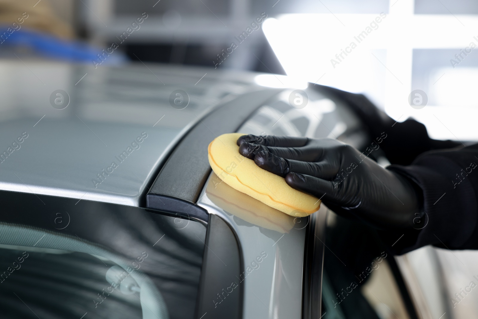 Photo of Man polishing car with yellow sponge indoors, closeup