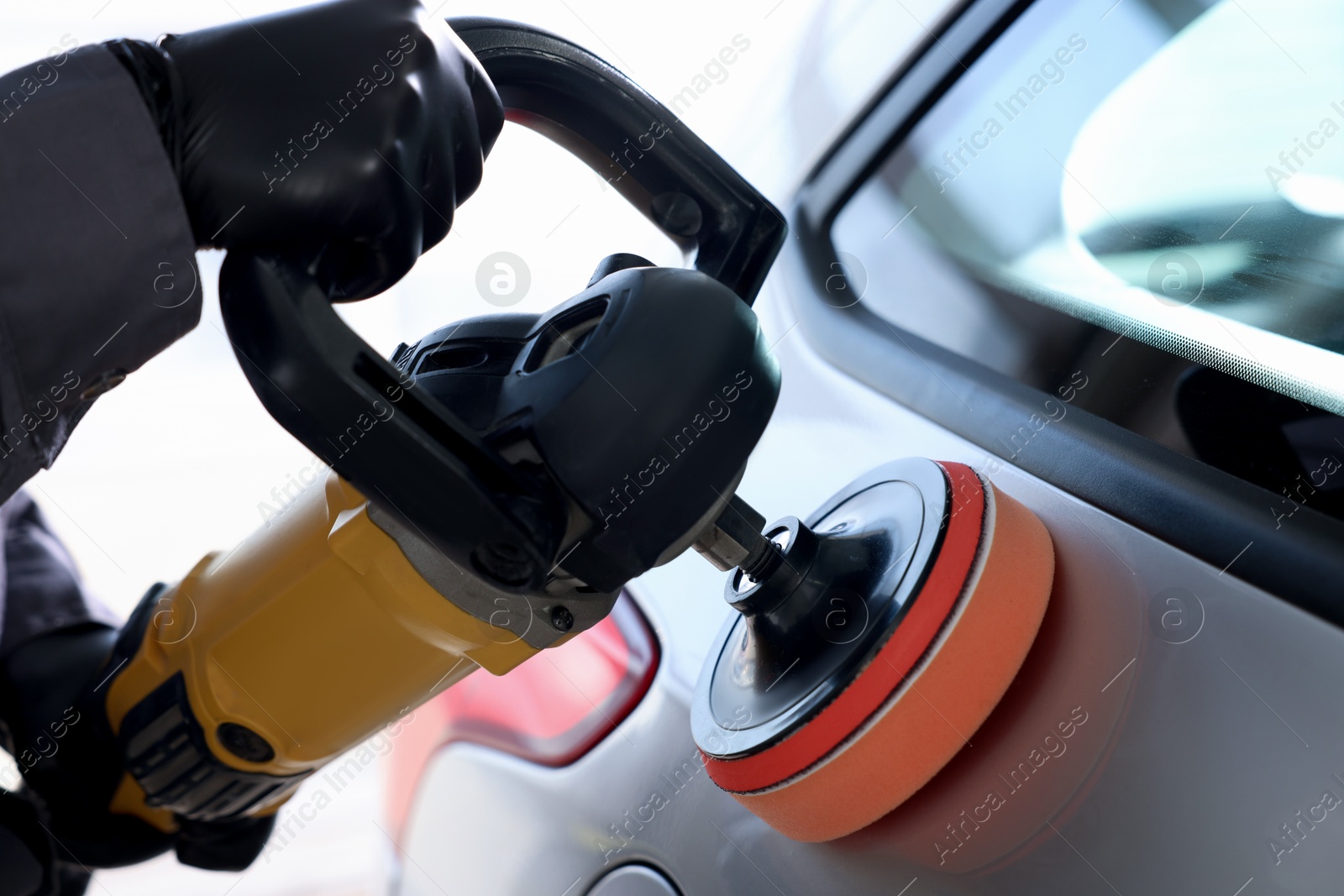 Photo of Man polishing car with orbital polisher indoors, closeup