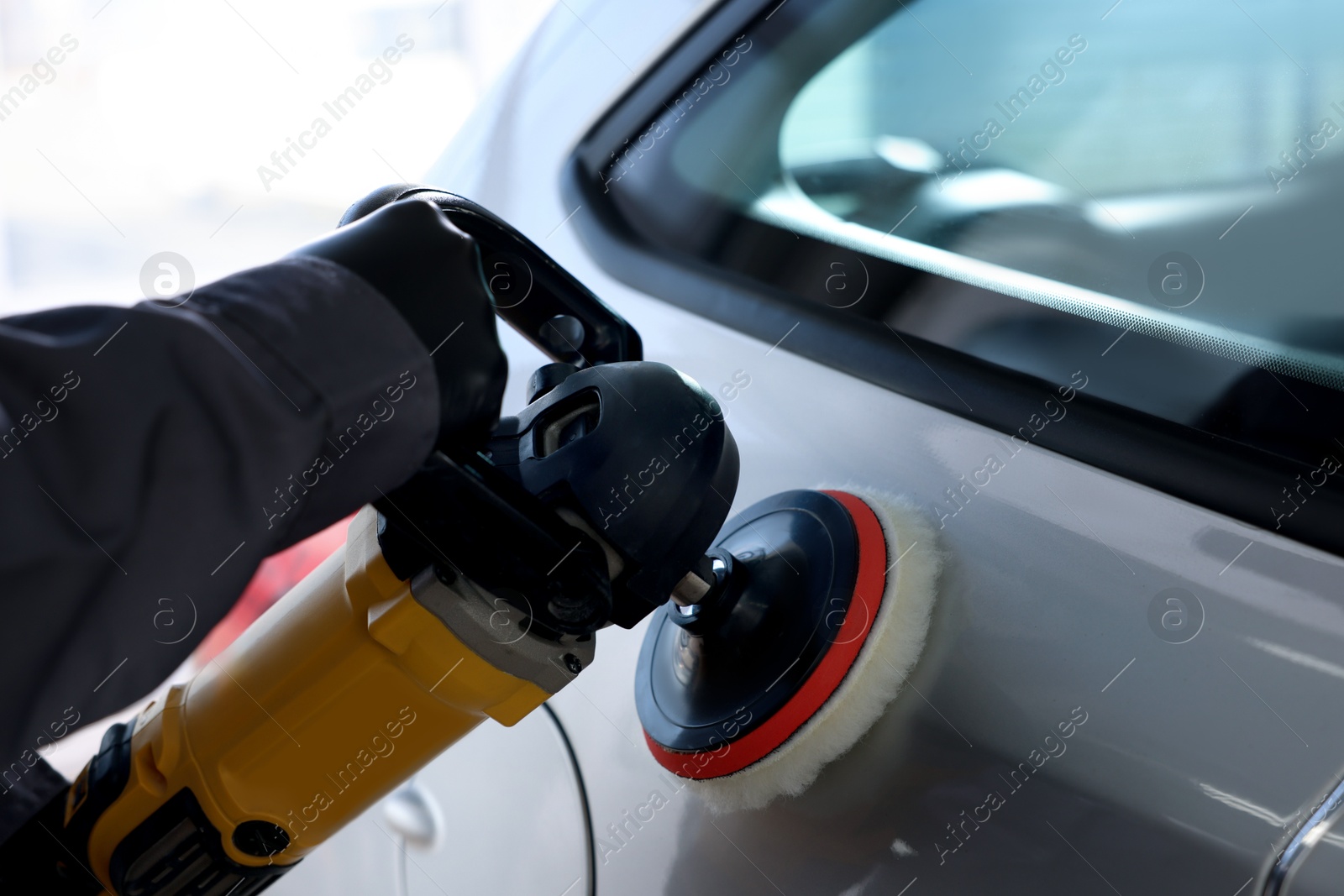 Photo of Man polishing car with orbital polisher indoors, closeup