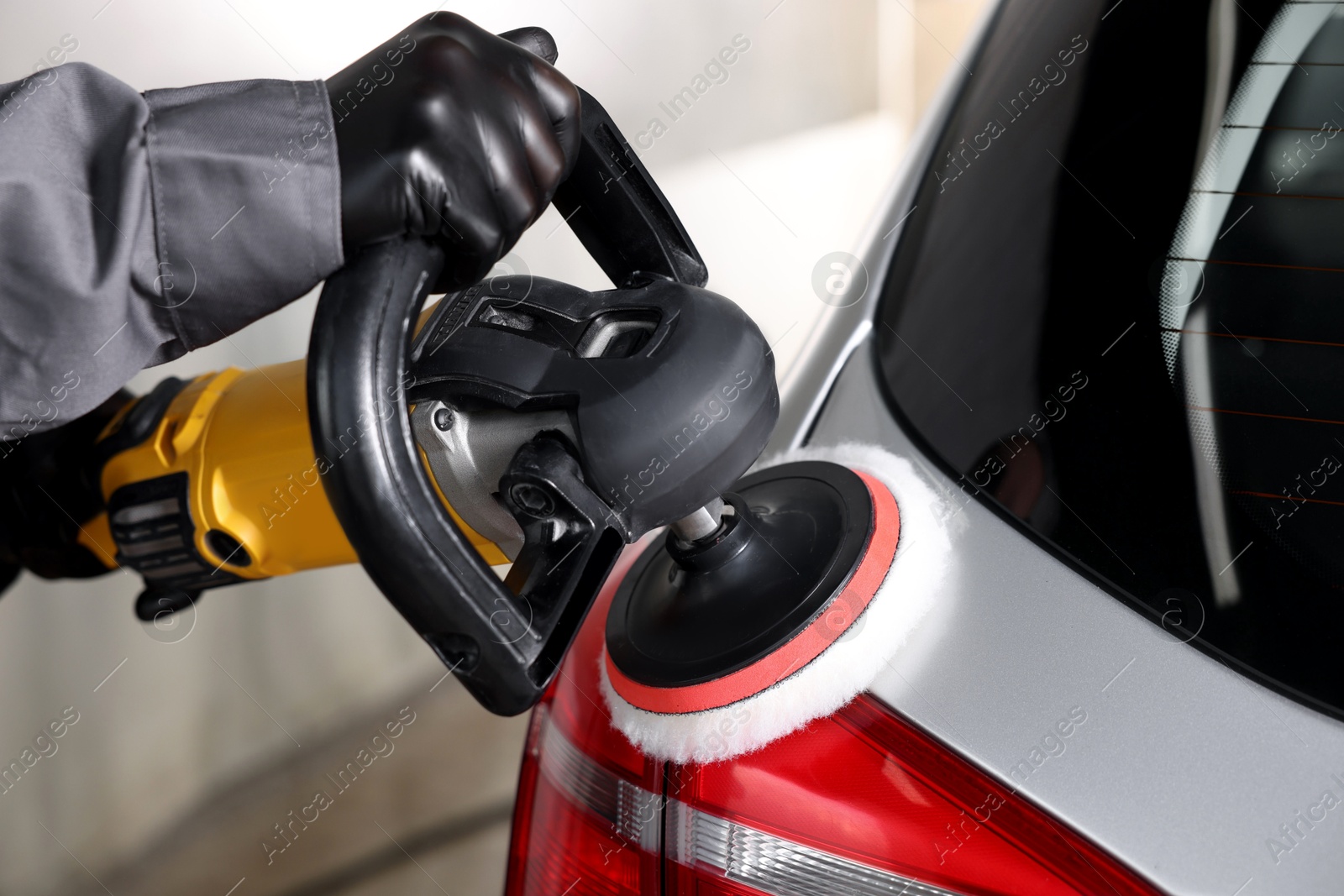 Photo of Man polishing car with orbital polisher indoors, closeup