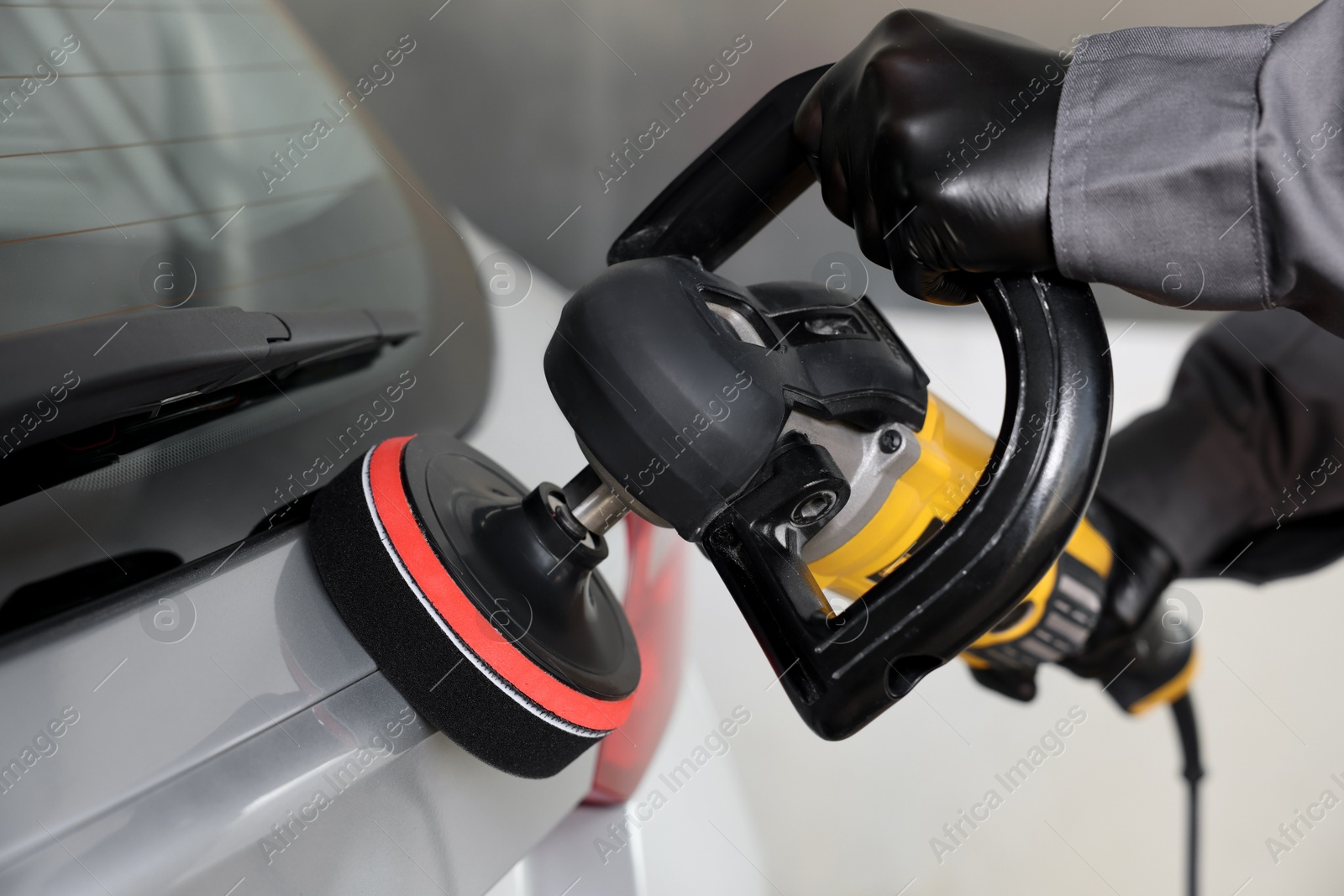 Photo of Man polishing car with orbital polisher indoors, closeup